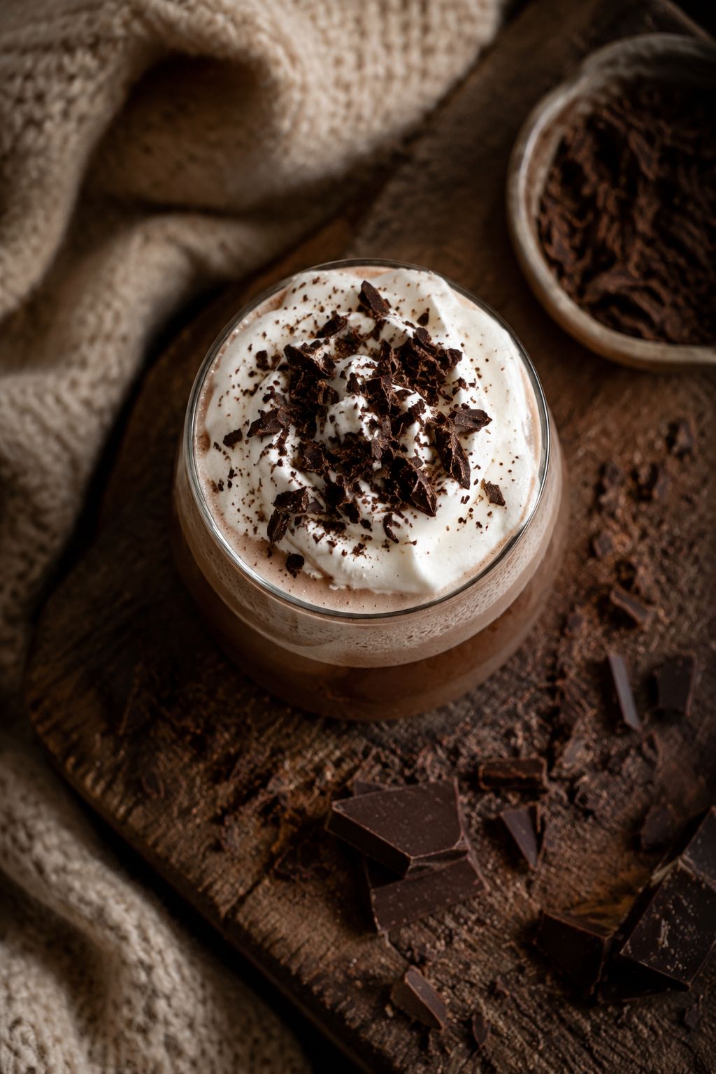 Bird's eye view of a glass of layered chocolate protein hot cocoa with whipped coconut cream on top, surrounded by dark