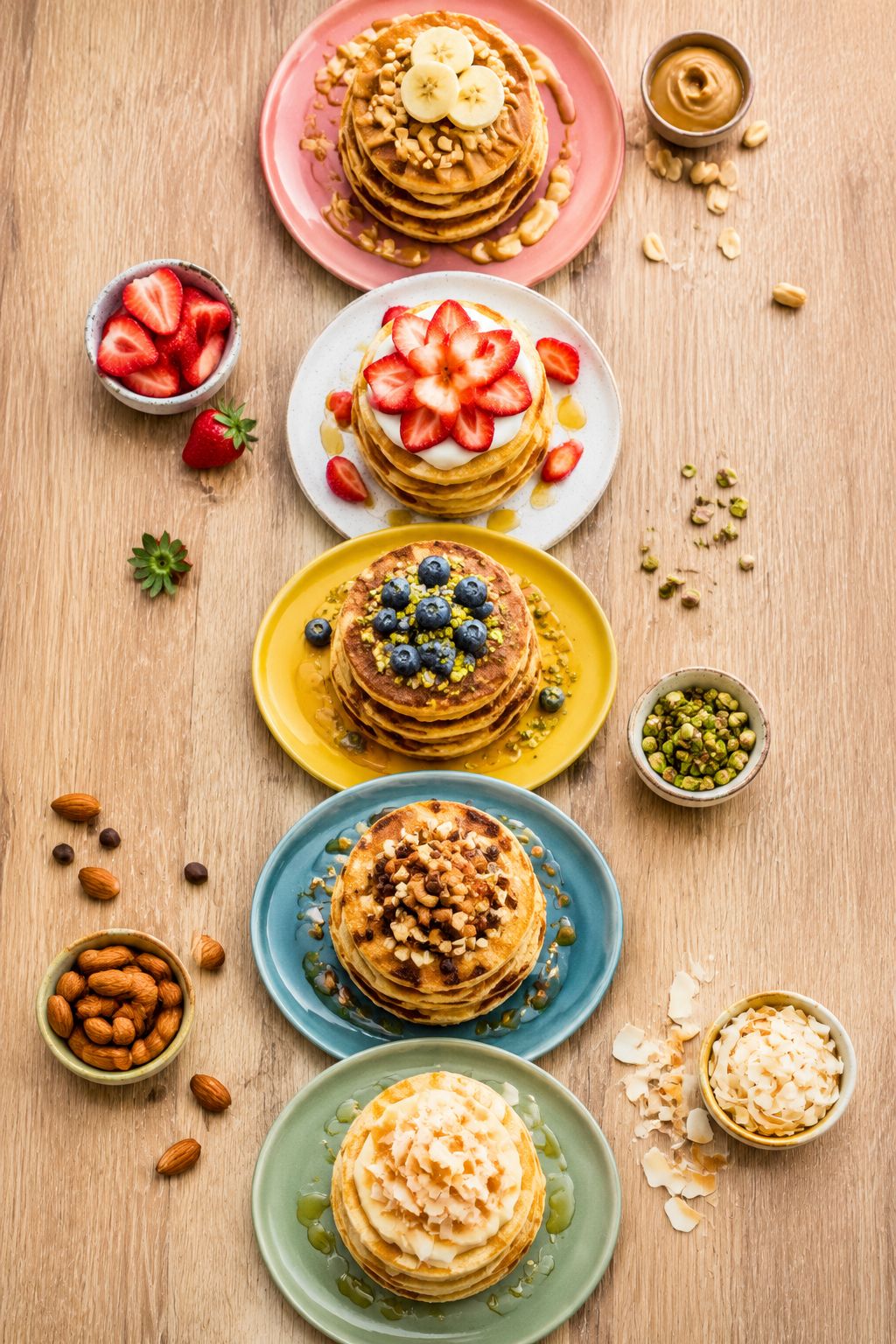 Portrait/Pinterest format () top-down flat lay of five distinct small pancake stacks arranged in a row on different colored